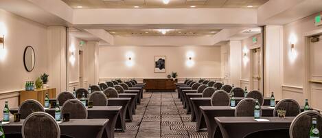 A conference room with rows of tables and chairs, equipped with water bottles and a podium at the front.