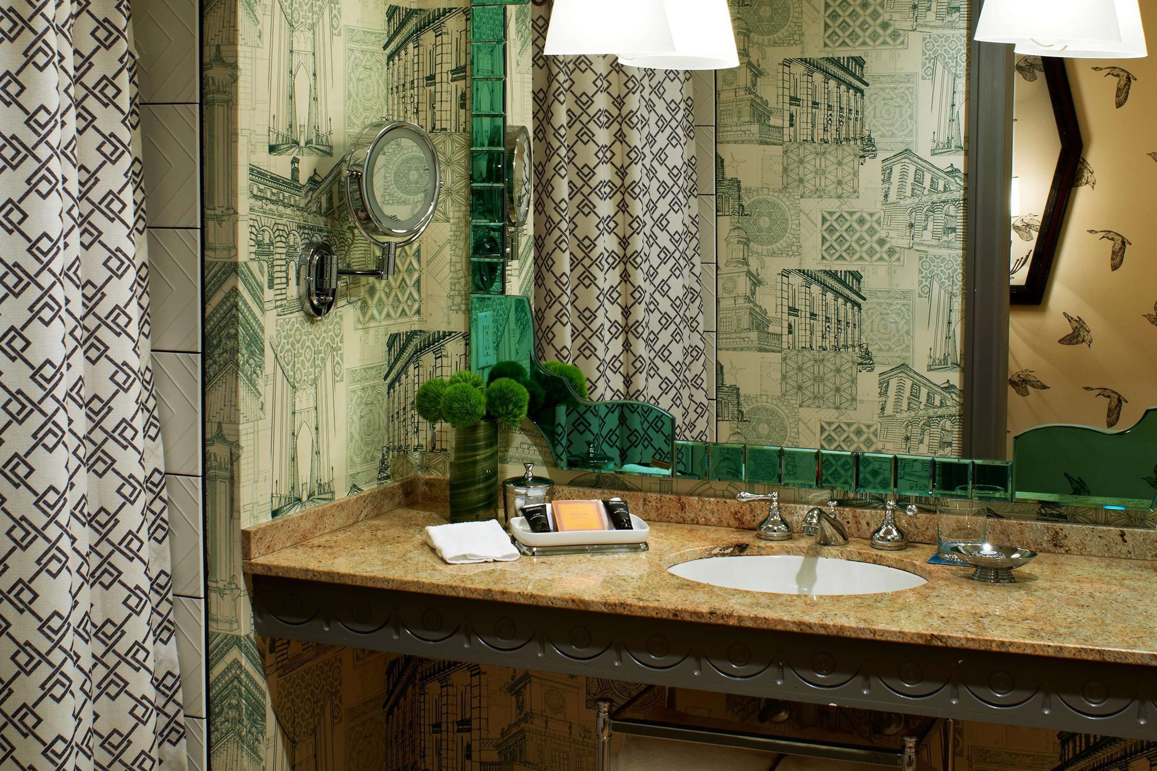A bathroom with a patterned wallpaper, a sink, a mirror, and a green plant.