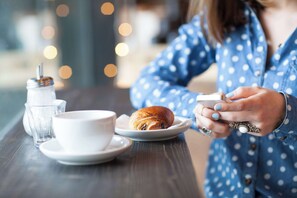 A person holding a smartphone at a table with a croissant, a cup, and a glass of water.