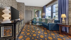 Ein modernes Wohnzimmer mit einem gemusterten Teppich, einem blauen Sofa, einem Glastisch und einem großen Fenster mit Blick auf die Stadt.
