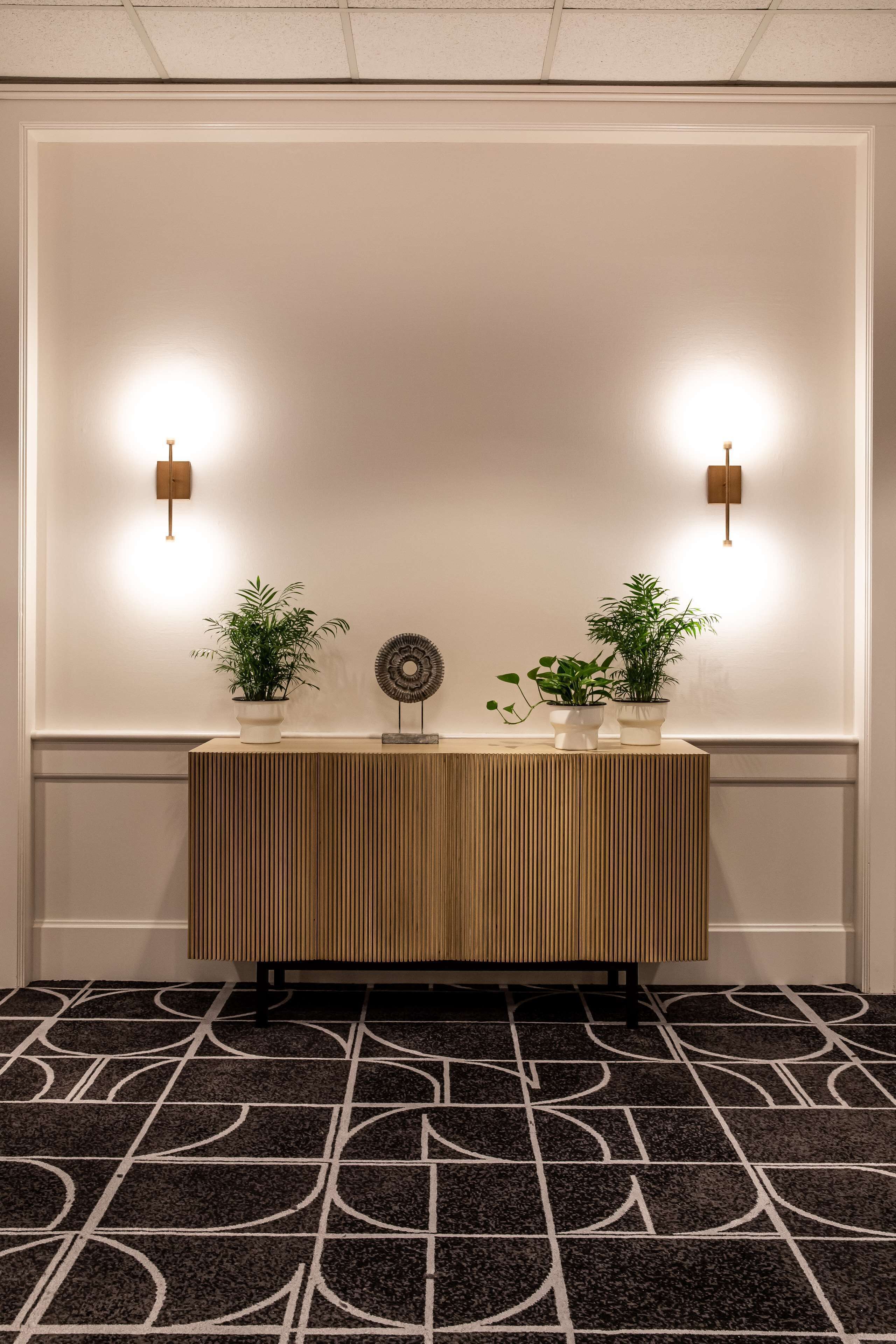 Un espace d’accueil avec une console en bois, deux plantes en pot et des luminaires fixés au mur.