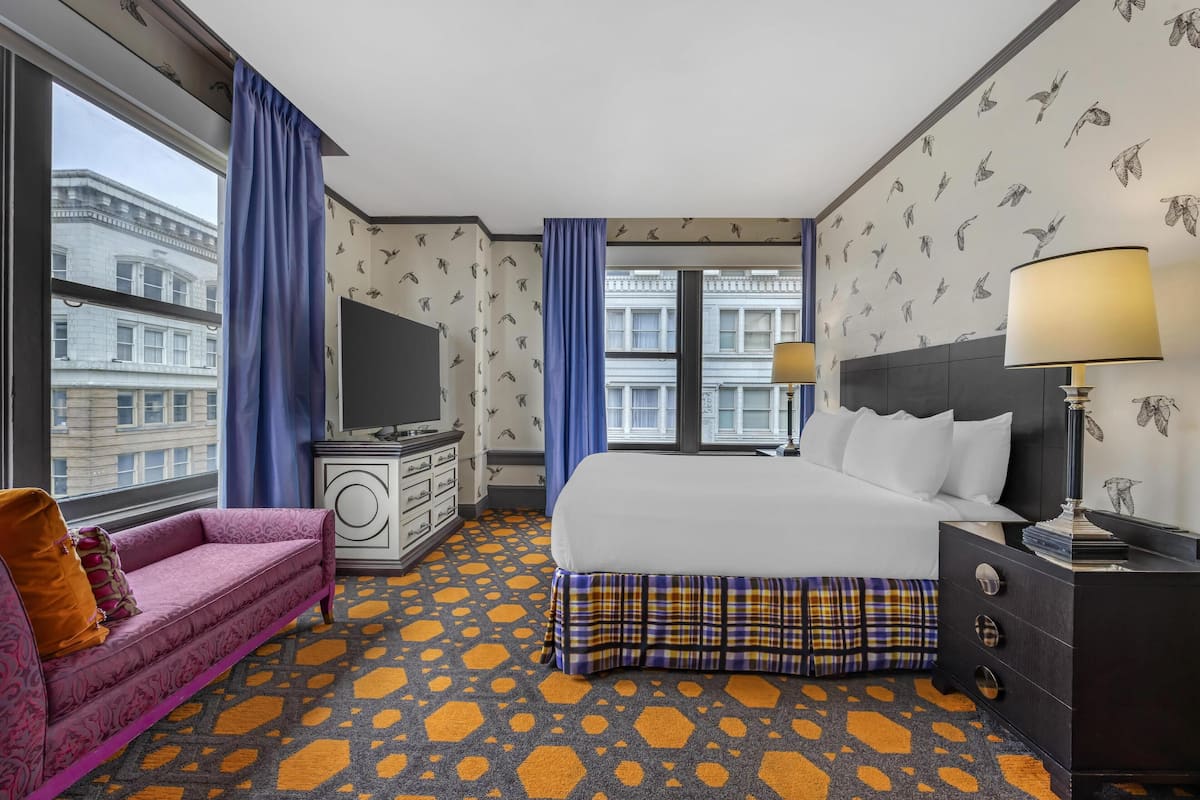 A hotel room with a bed, a sofa, a dresser, a TV, and a window with curtains.