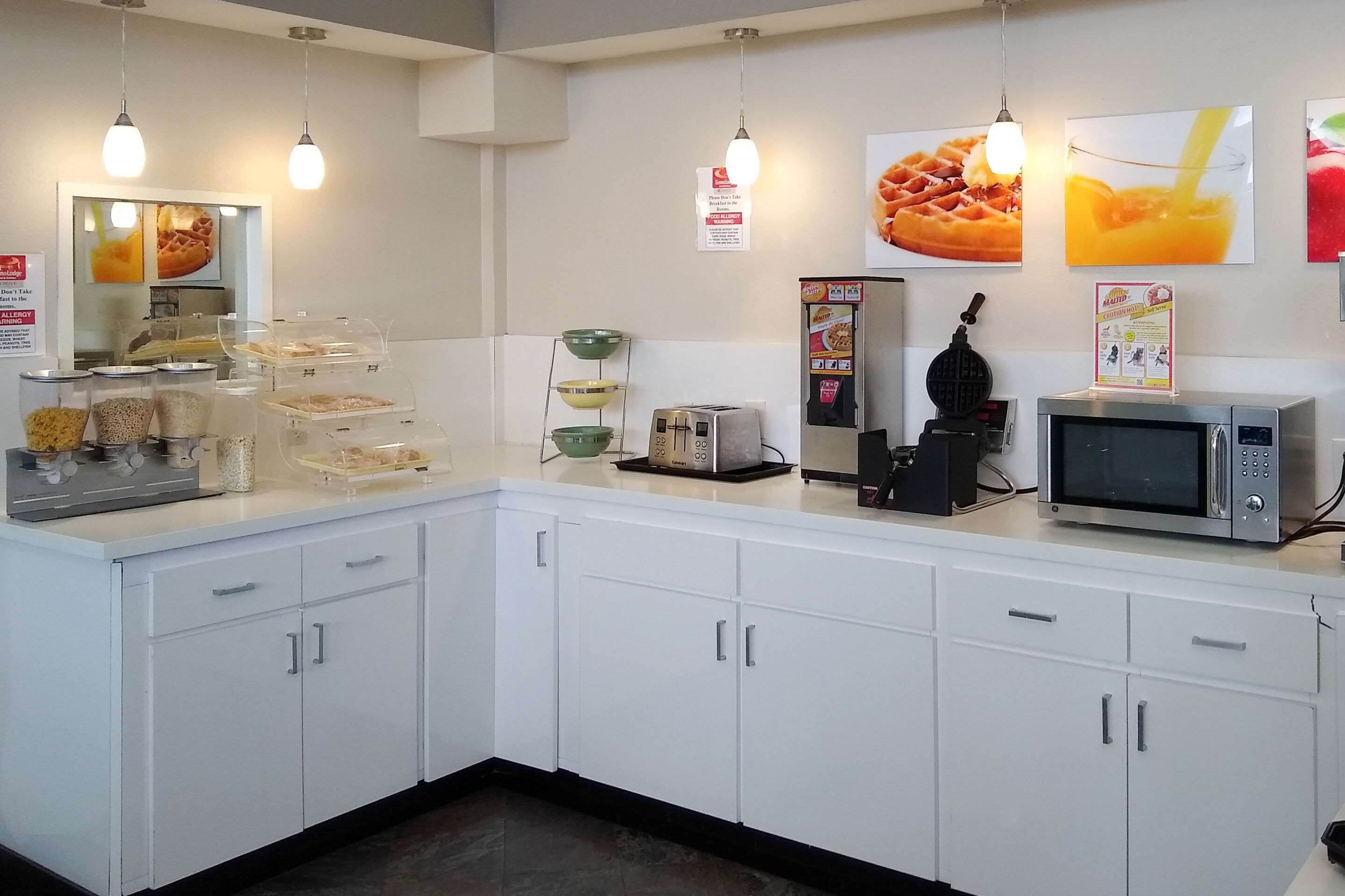 Een keukenhoek met witte kastjes, een magnetron, een broodrooster en diverse bakjes voor eten.