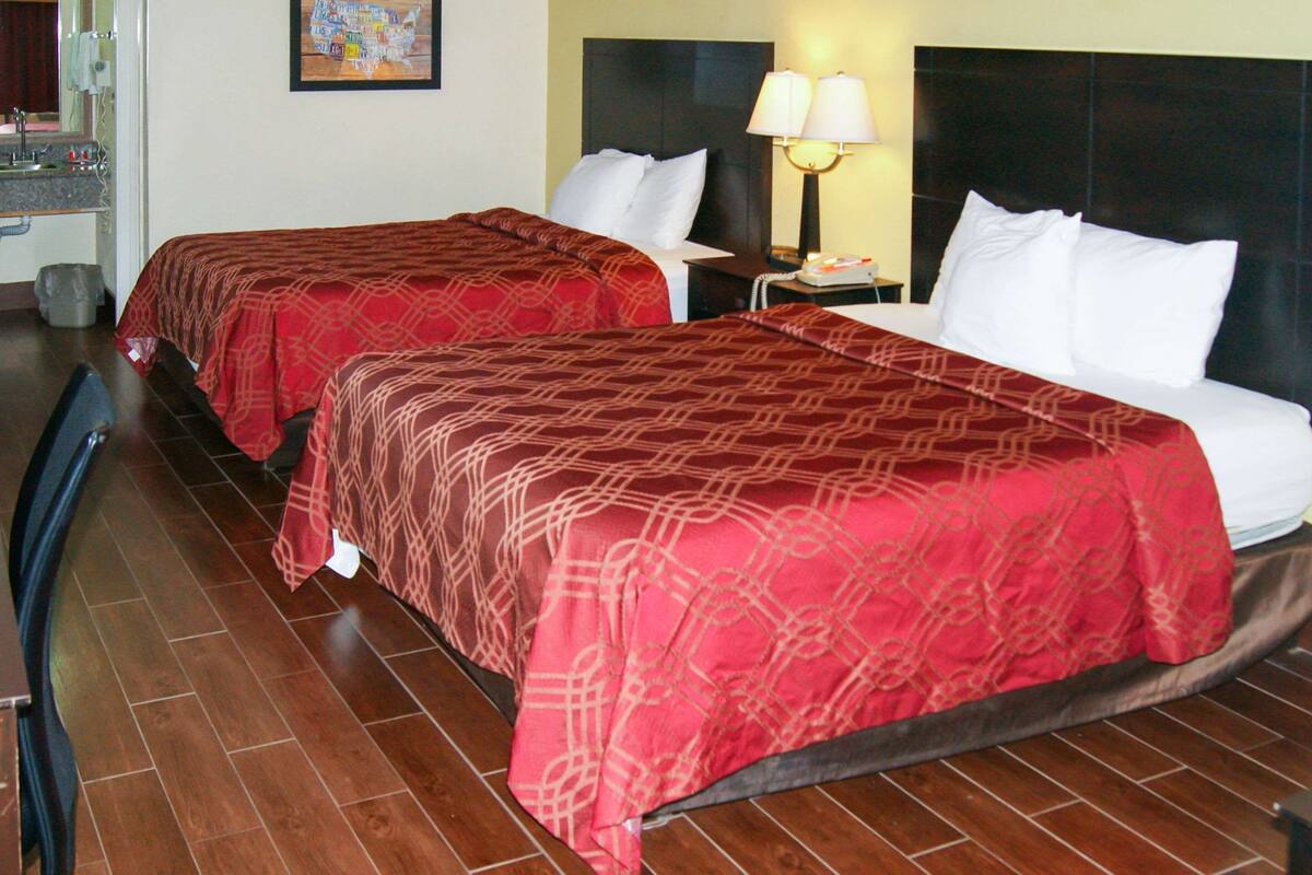 Une chambre d’hôtel avec deux lits, chacun recouvert d’une couvre-lit à motifs rouges, une table de chevet avec une lampe et un plancher en bois.