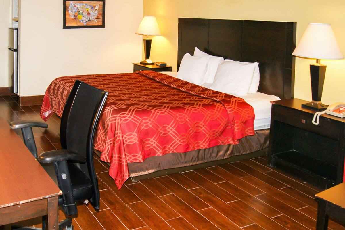 Une chambre d’hôtel comprenant un lit, deux tables de chevet avec des lampes, une chaise, un bureau et une cheminée.
