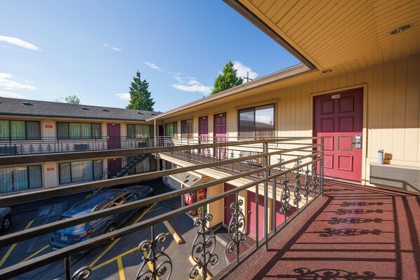 A motel with a parking lot, a red door, and a balcony with a metal railing.