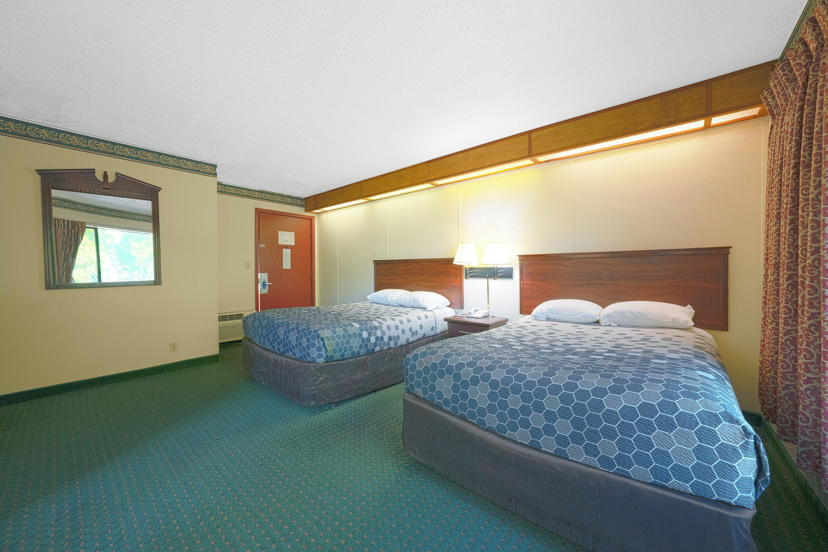 A hotel room with two beds, a nightstand, a lamp, and a window with curtains.