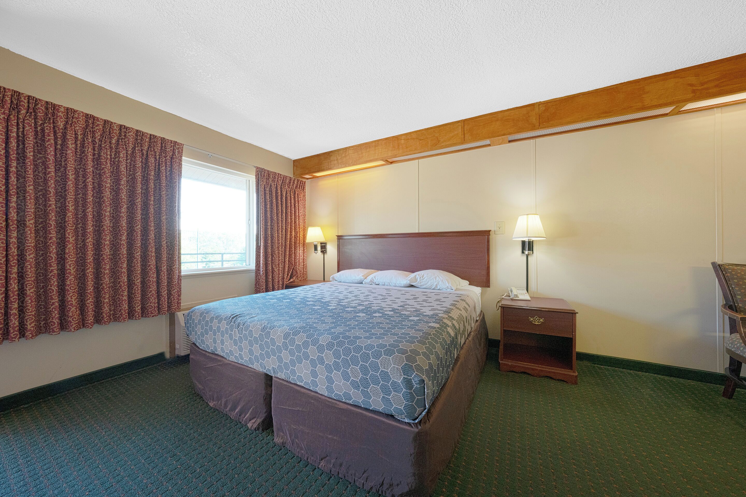 Quarto de hotel com uma cama grande, duas luminárias de cabeceira, um painel de cabeceira de madeira e uma janela com cortinas.