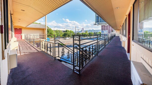 A covered outdoor corridor with a view of a parking lot and cityscape. - Broadway Inn (Portland)