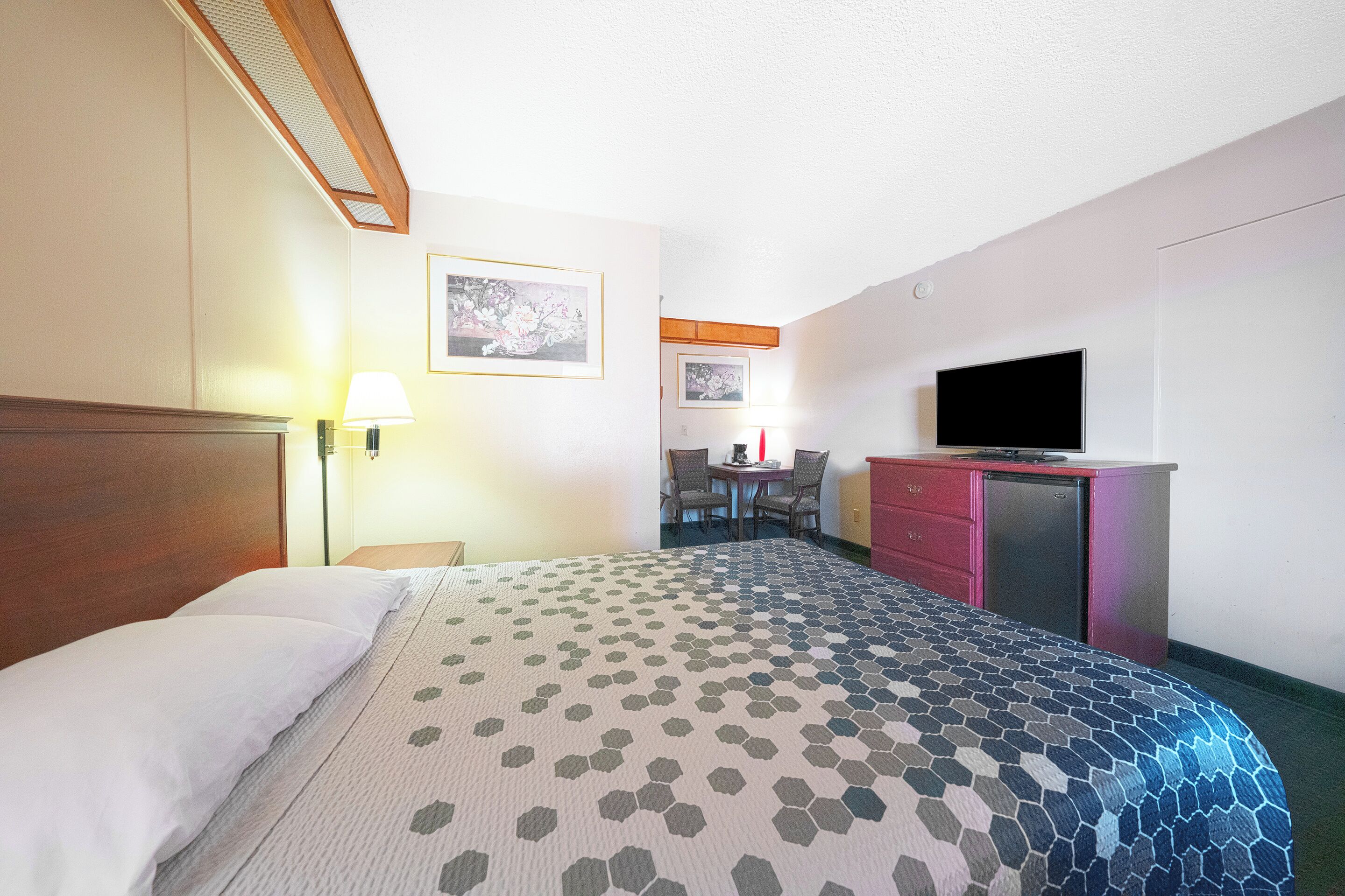 A hotel room with a bed, a desk, a television, and a small kitchenette.