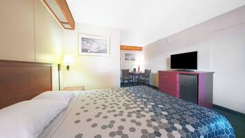 A hotel room with a bed, a desk, a television, and a small kitchenette.