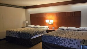 A hotel room with two beds, each with a patterned bedspread, a nightstand with a lamp, and a wooden headboard. - Broadway Inn (Portland)