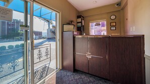 A reception area with a glass door, a wooden reception desk, a clock, and framed certificates on the wall. - Broadway Inn (Portland)