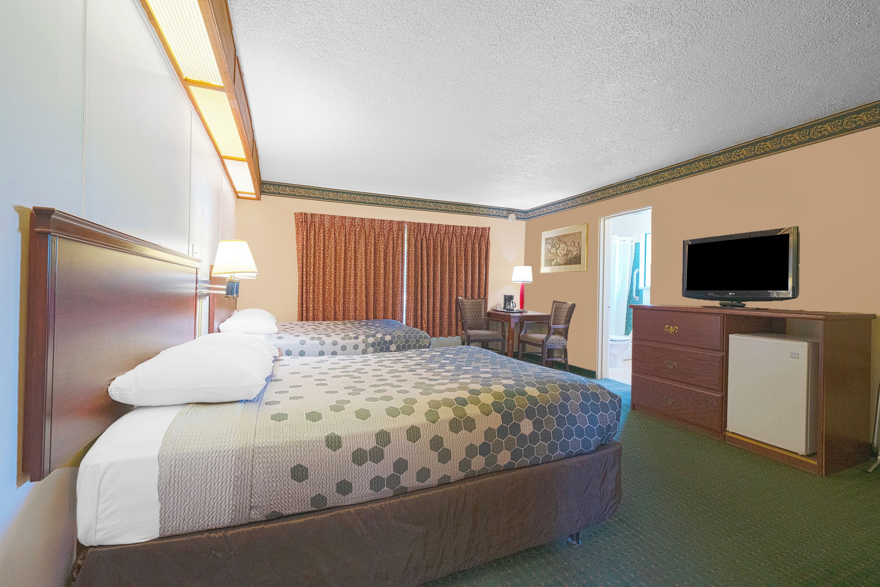 A hotel room with two beds, a desk, a television, and a refrigerator.
