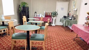 A dining area with round tables and chairs, a patterned carpet, and a refrigerator in the background. - Americas Best Value Inn & Suites Houston Brookhollow NW (Houston)