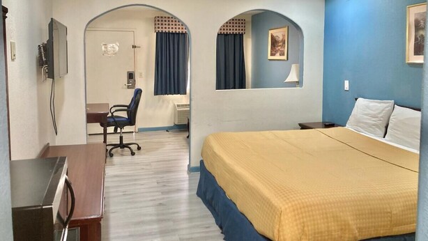 A hotel room with a bed, desk, chair, and an arched doorway. - Americas Best Value Inn & Suites Houston Brookhollow NW (Houston)