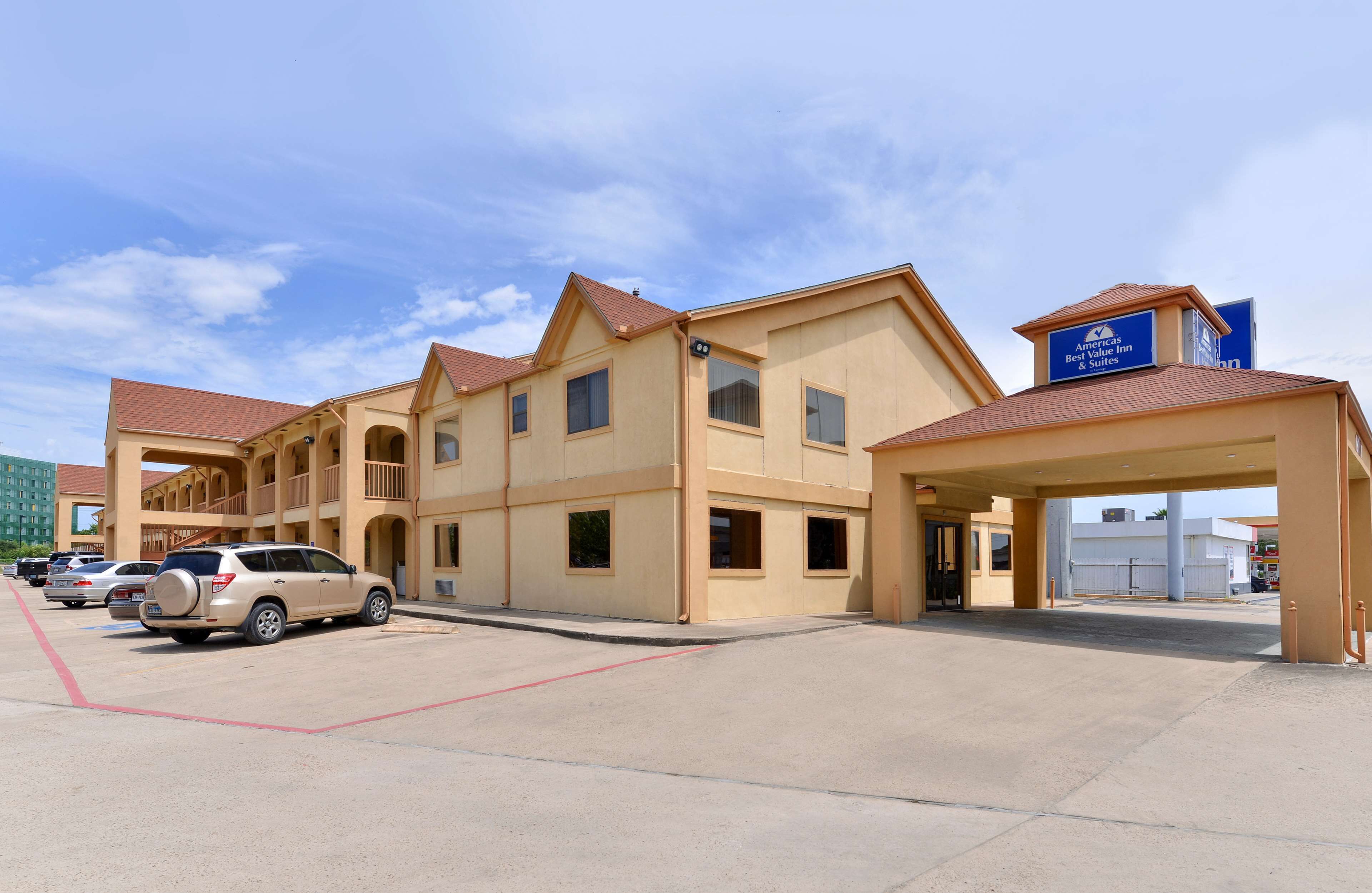 A hotel with a two-story structure, a covered entrance, and a parking lot with several cars.