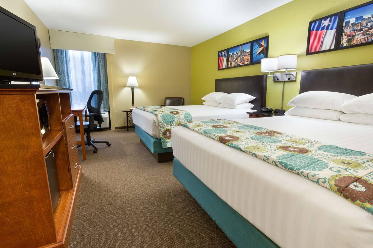 A hotel room with two beds, a desk with a television, a chair, and a lamp.