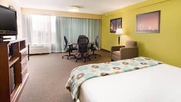A hotel room with a bed, a desk with a chair, a television, and a cityscape painting on the wall.