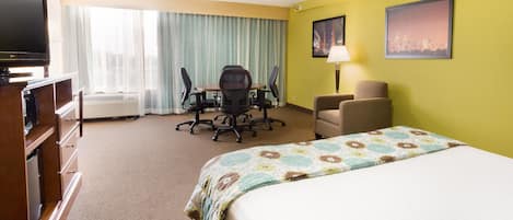 A hotel room with a bed, a desk with a chair, a television, and a cityscape painting on the wall.