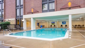 An indoor swimming pool with a clear blue water, surrounded by lounge chairs and a brick building in the background.