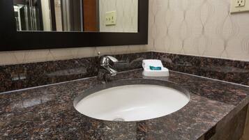 Baño con encimera de granito, lavamanos blanco, espejo y dispensador de toallas.