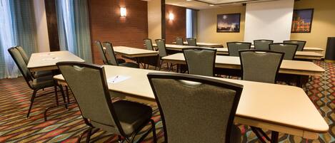 A conference room with multiple tables and chairs, a projector screen, and a patterned carpet.