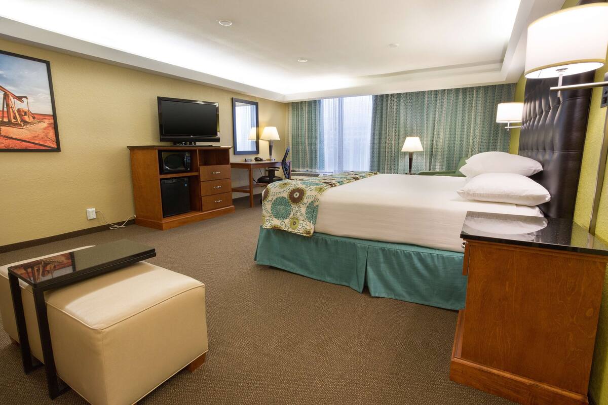 A hotel room with a bed, a desk with a computer, a television, and a small table.