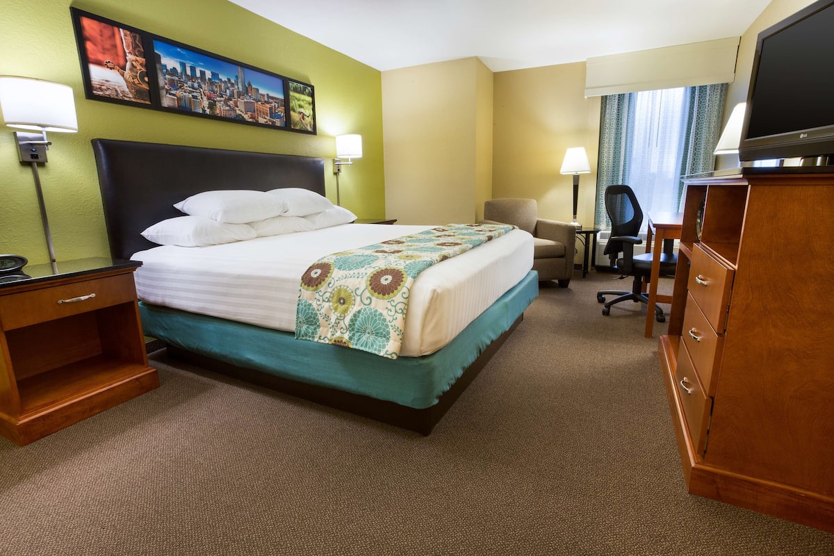 A hotel room with a bed, a desk, a chair, a TV, and a painting on the wall.