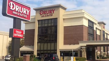 A Drury Inn & Suites building with a prominent entrance sign, a parking lot, and a clear sky.