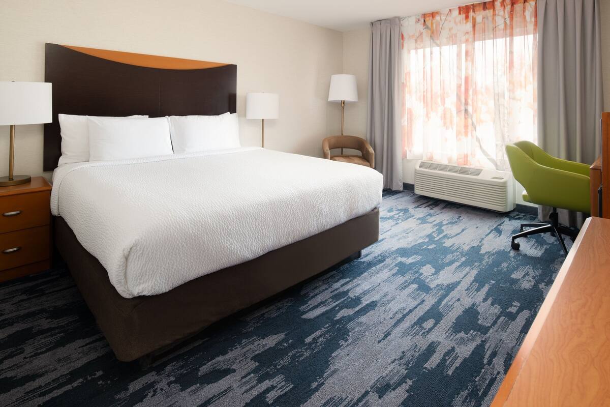 A hotel room with a large bed, a desk, a chair, and a window with curtains.