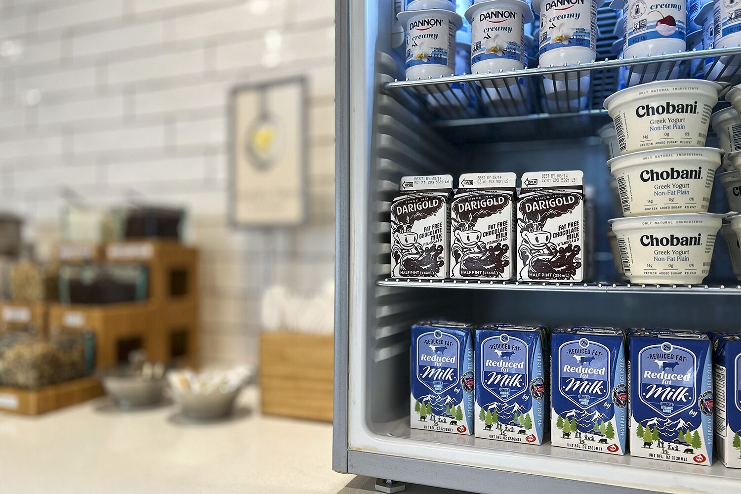 A refrigerated display of various dairy products including Dannon cream, Chobani Greek yogurt, Darigold fat-free chocolate milk, and reduced-fat milk.