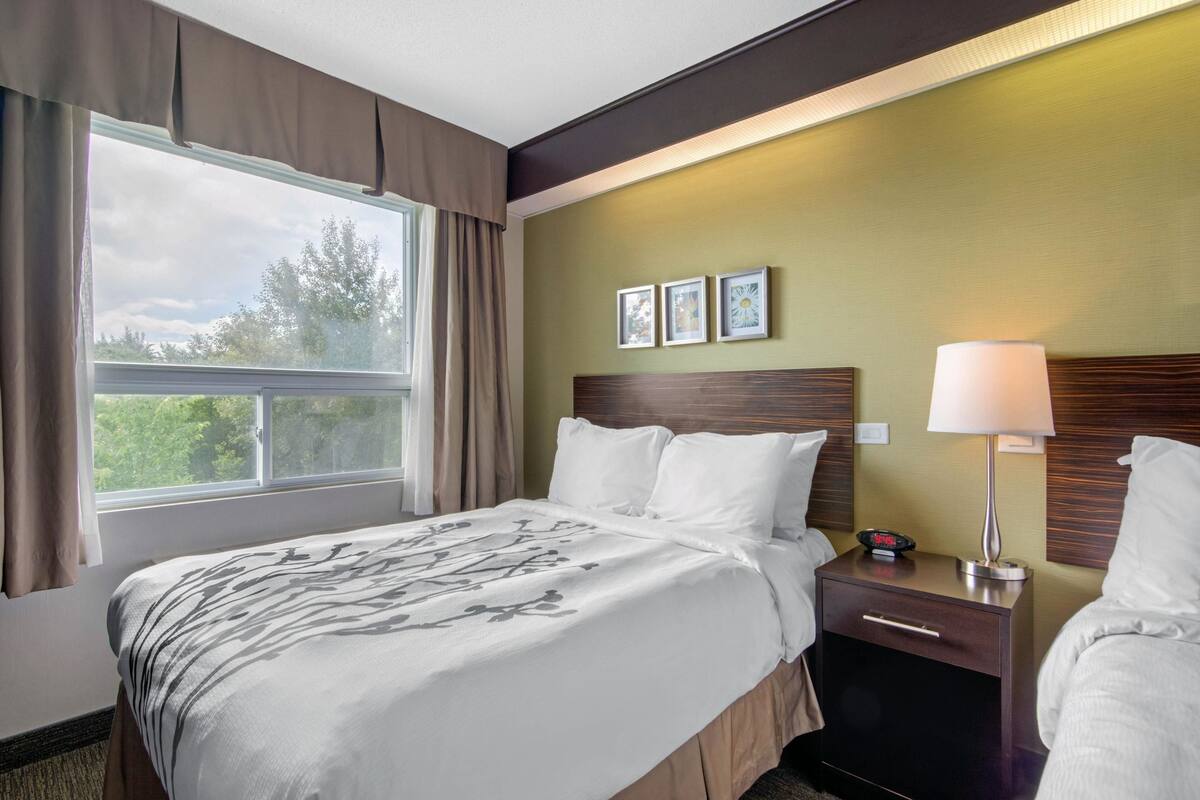 Une chambre d’hôtel avec un lit, une table de chevet, une lampe et une fenêtre avec des rideaux.