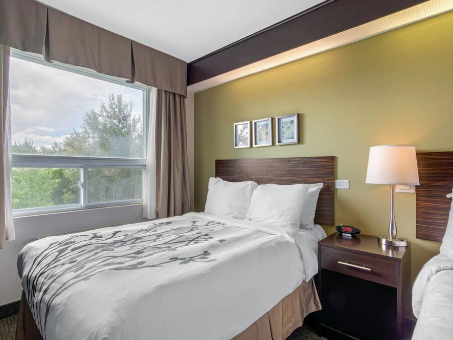 Una habitación de hotel con una cama, una mesita de noche, una lámpara y un ventanal con cortinas.