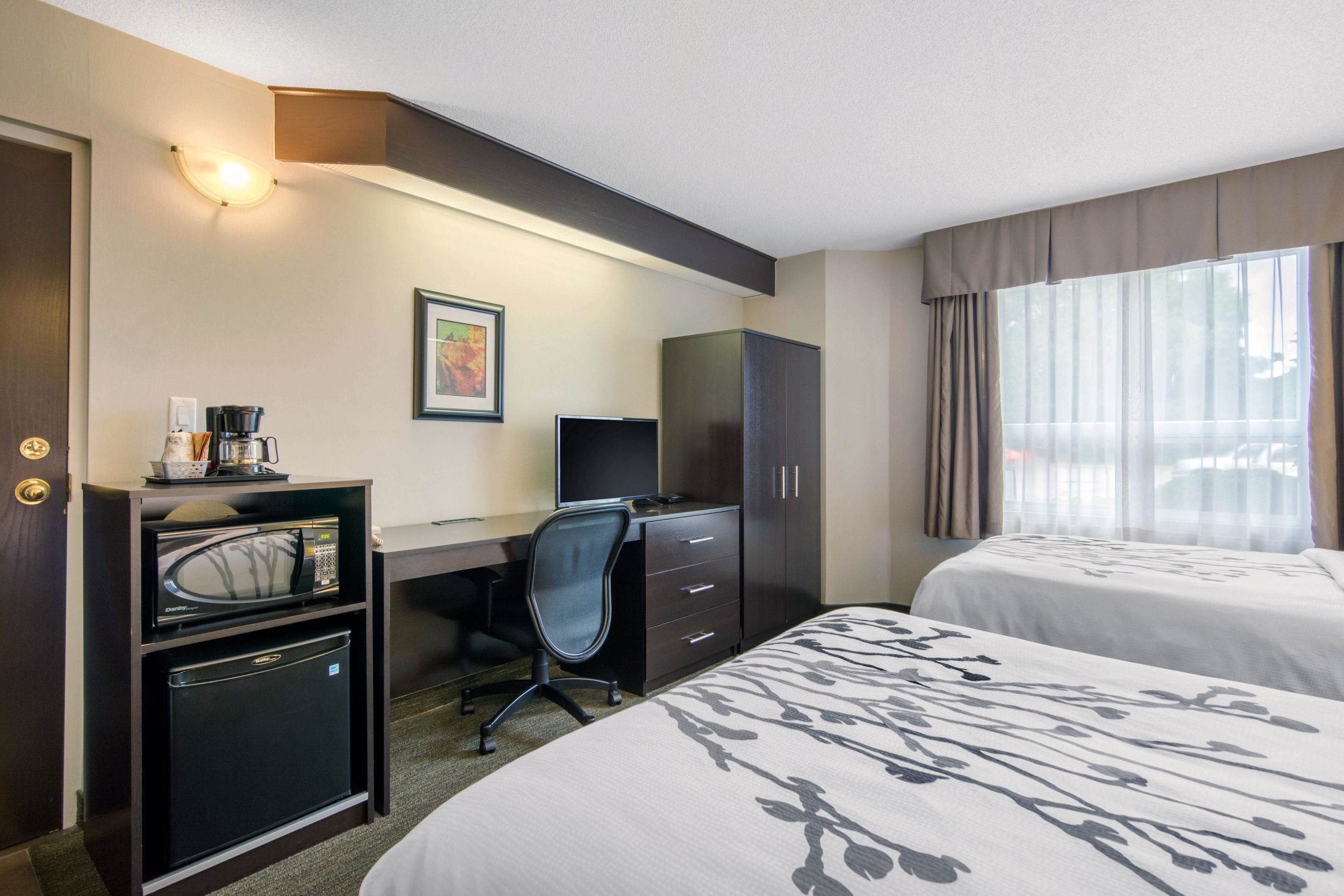 A hotel room with two beds, a desk with a computer, a microwave, and a refrigerator.
