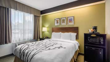 Hotelkamer met een bed, nachtkastje, lamp, magnetron en raam met gordijnen.