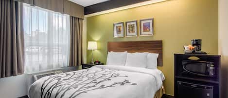 Una habitación de hotel con cama, mesita de noche, lámpara, microondas y ventana con cortinas.