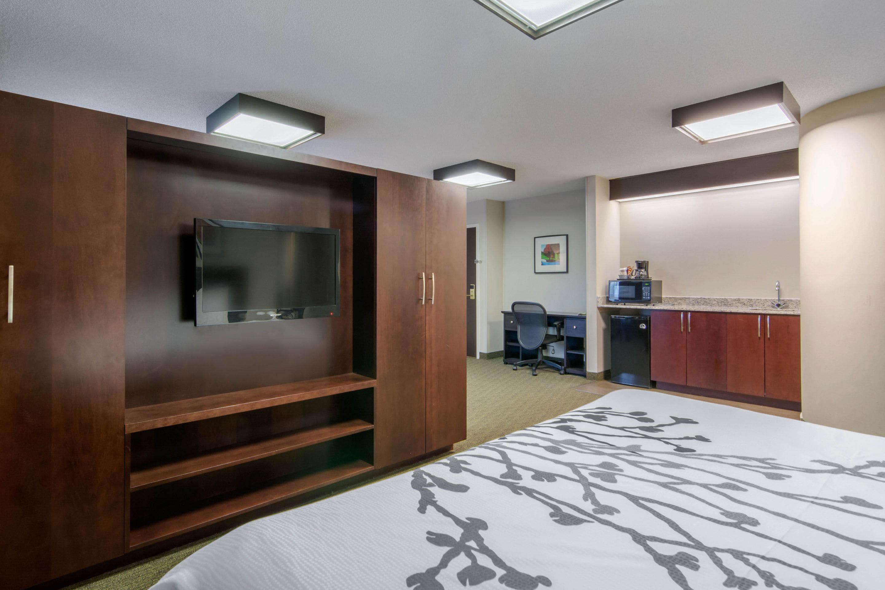A hotel room with a bed, a TV, a desk, and a kitchenette.