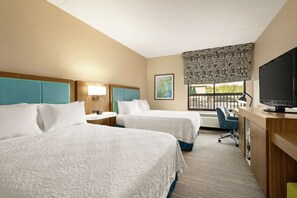 A hotel room with two beds, a desk with a television, a chair, a window with a view, and a painting on the wall.