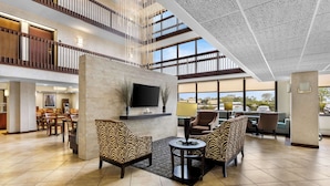 A spacious lobby with a high ceiling, a TV mounted on a stone wall, and a seating area with patterned chairs. - Sonesta Essential Houston Hobby Airport (Houston)