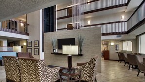 A spacious lobby with a high ceiling, a central seating area with patterned chairs, a round table, and a flat-screen TV mounted on the wall. - Sonesta Essential Houston Hobby Airport (Houston)