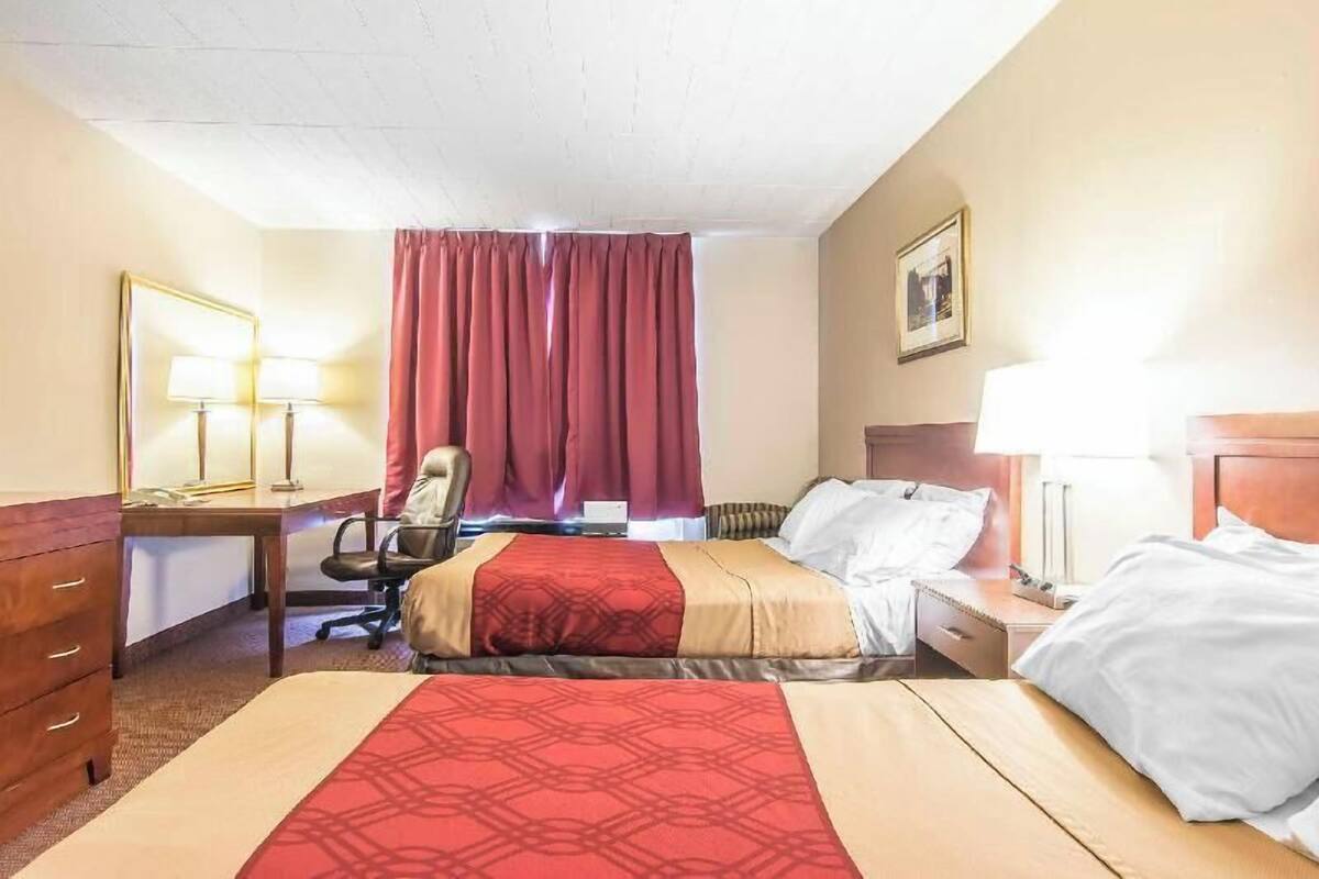 A hotel room with two beds, a desk, a chair, and a window with curtains.