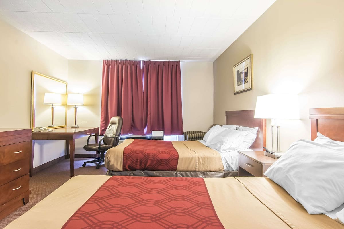 A hotel room with two beds, a desk, a chair, a lamp, and a large window with curtains.