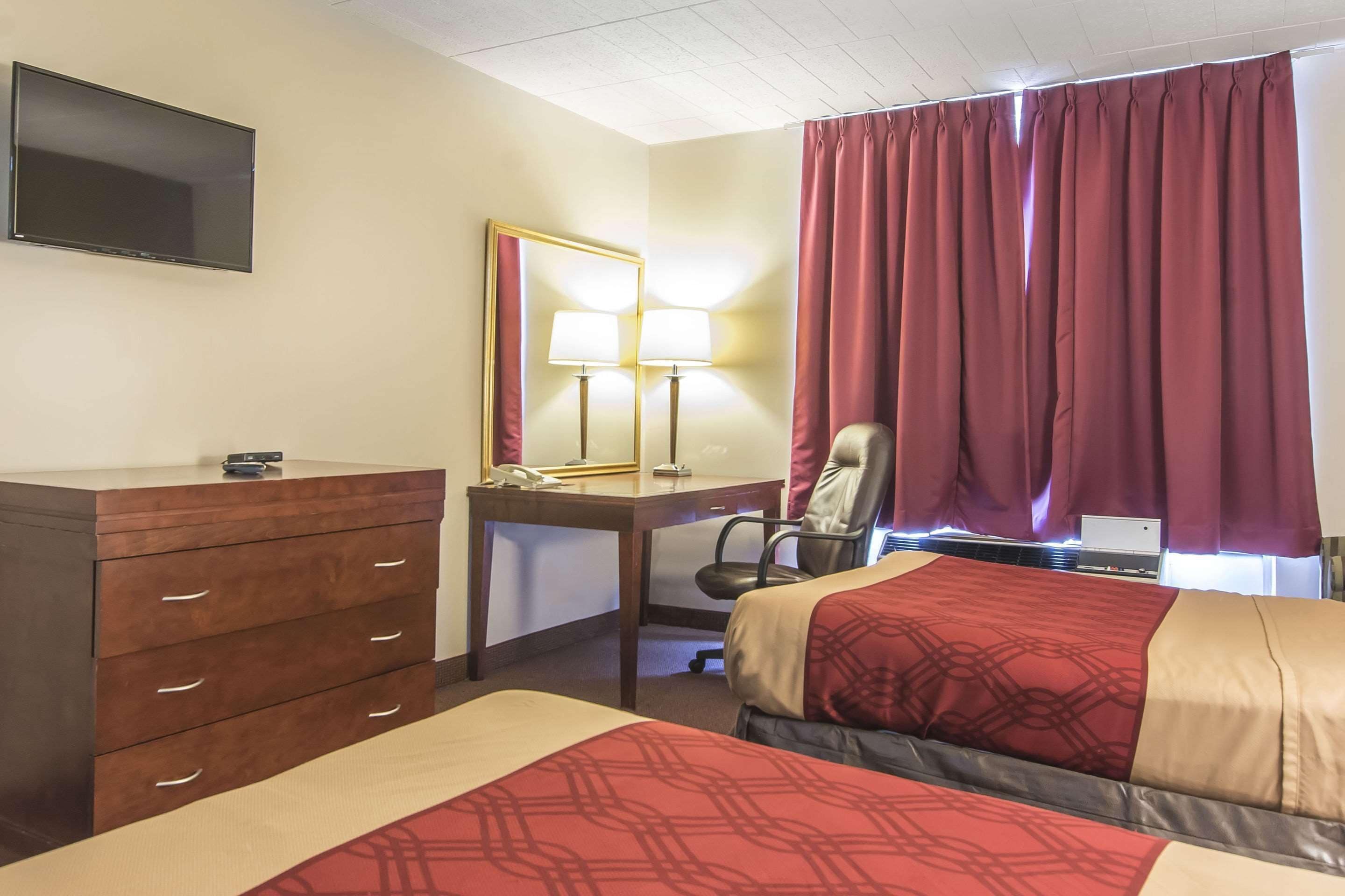 Habitació d'hotel amb dos llits, un escriptori, una cadira, un televisor i una finestra amb cortines.
