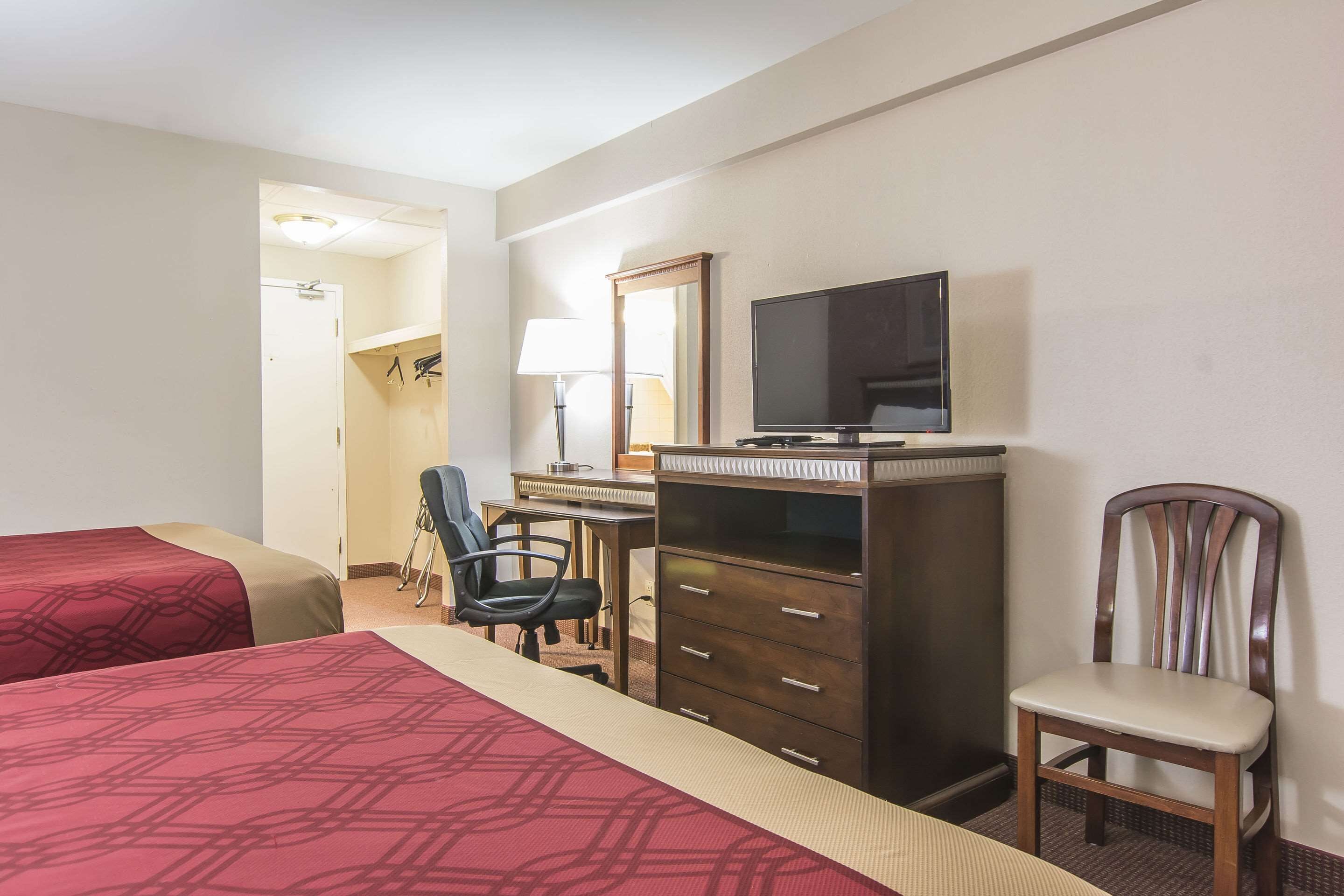 A hotel room with two beds, a desk with a computer, a chair, a television, and a wardrobe.
