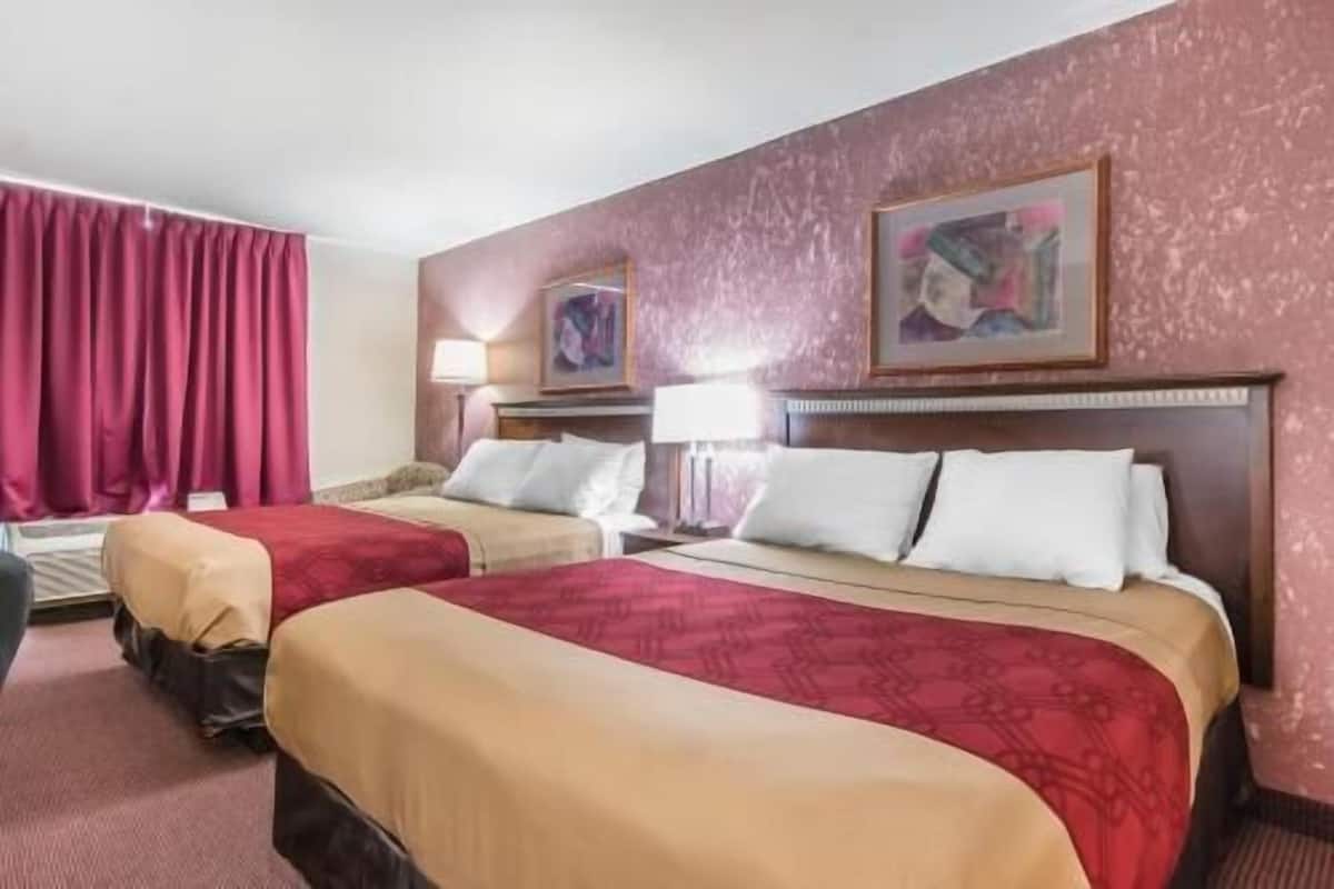 A hotel room with two beds, a desk, a chair, and a window with curtains.