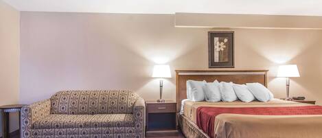 Ein Hotelzimmer mit einer gemusterten Couch, einem Bett mit roter Decke, zwei Nachttischen mit Lampen und einem gerahmten Bild an der Wand.
