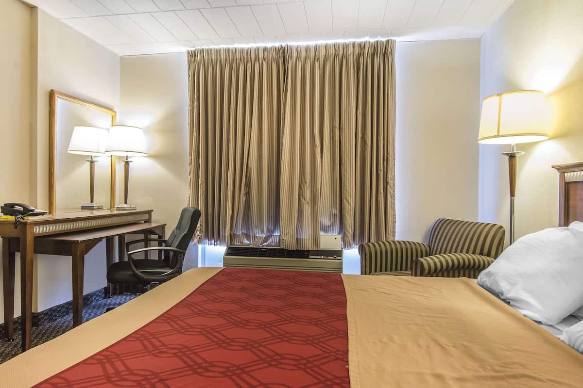 A hotel room with a large bed, a desk with a telephone, two chairs, a window with curtains, and two lamps.