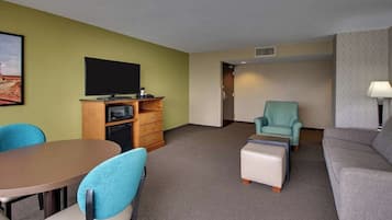 A hotel room with a dining table, chairs, a sofa, a TV, and a microwave.