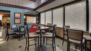 A hotel lobby with a mix of seating options, including round tables and chairs, and a large window offering a view of the outdoors. - Heritage Inn & Suites The Woodlands, Trademark by Wyndham (The Woodlands)